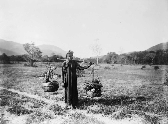 Người phụ nữ gồng gánh ra chợ với đứa con ngồi ở một bên quang gánh, phía Nam Cam Ranh.