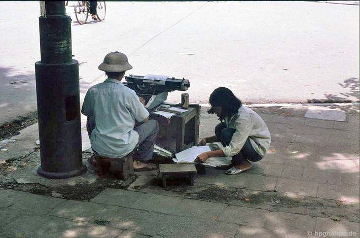 Một người đàn ông ngồi đánh máy chữ ở một ngã tư của khu phố cổ Hà Nội năm 1991. Nghề đánh máy chữ ở Hà Nội đầu thập niên 1990 đã biến mất cùng sự hiện diện của các cửa hàng photocopy, in vi tính. Ảnh: Hans-Peter Grumpe/Hpgrumpe.de.
