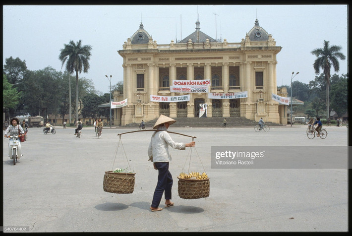 Một người phụ nữ gánh chuối qua Quảng trường Cách Mạng Tháng Tám, Hà Nội năm 1991. Ảnh: Vittoriano Rastelli/CORBIS/Corbis via Getty Images.