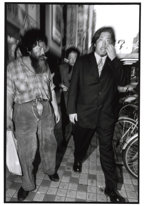 Một thành viên Yakuza đi ngang qua một người vô gia cư ở khu trung tâm tài chính Shinjuku, Tokyo. Ảnh: Bruce Gilden/ Magnum Photos.