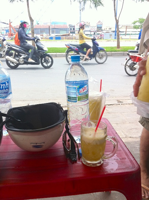 "Tôi lặng lẽ nhâm nhi nước mía khi ngắm nhìn xe máy qua lại trên đường. Xe máy ở Việt Nam nhiều vô kể. Nhiều người sẵn sàng tạt vào lể đường để mua một cốc nước mía mà mang nó đi bằng túi nhựa, như cốc ở trên". Ảnh: Kayoko Akabori.