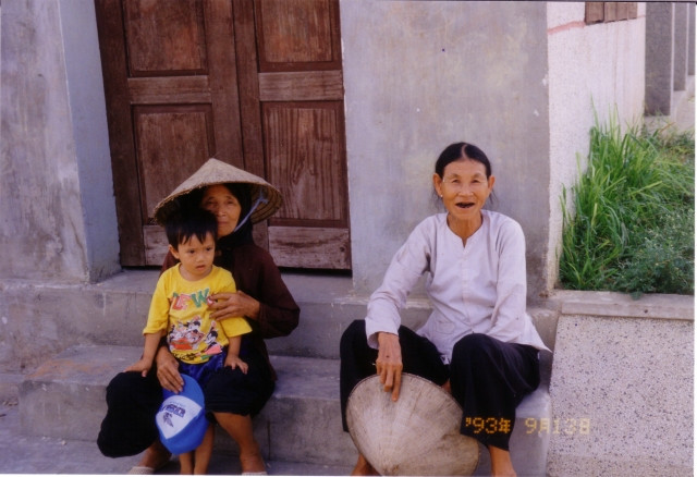 Hai cụ bà và em bé trước hiên nhà.