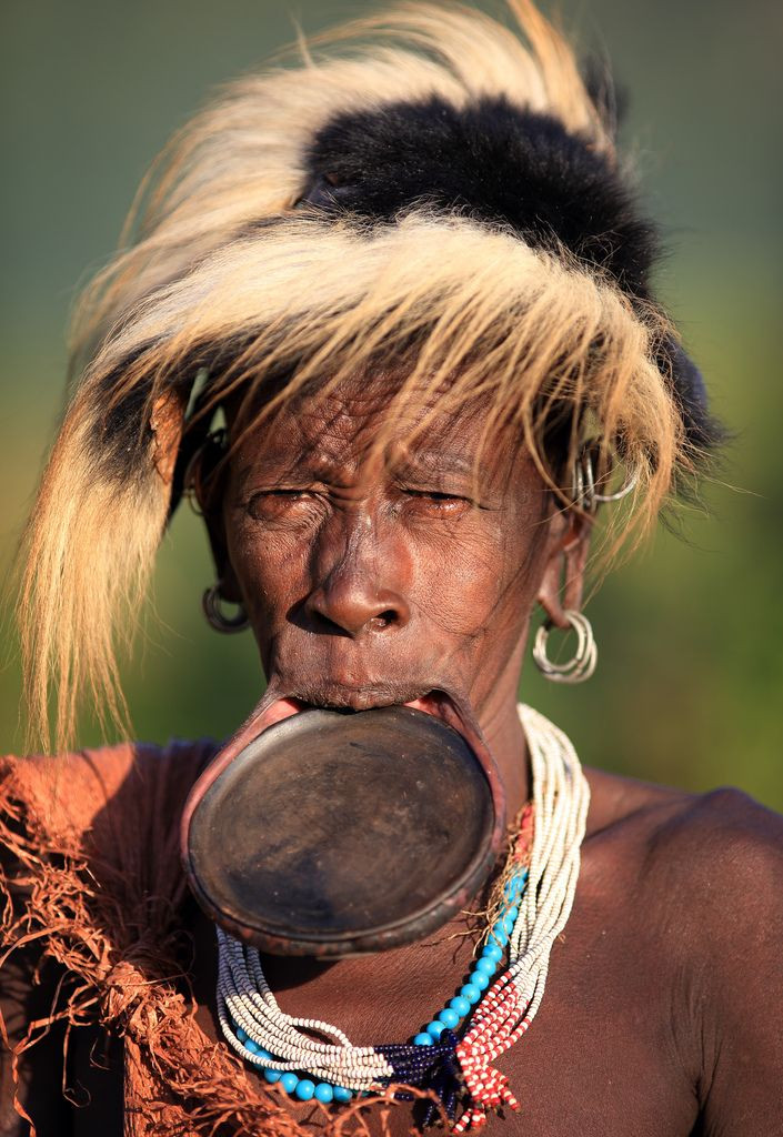 Bộ tộc Suri (Ethiopia) - Đĩa môi. Phụ nữ bộ tộc Suri nổi tiếng với tập tục đeo đĩa môi lớn. Khi đến tuổi trưởng thành, các cô gái sẽ được xỏ lỗ và dần dần kéo giãn môi để đeo những chiếc đĩa đất sét. Kích thước đĩa càng lớn thì càng được xem là đẹp và tôn trọng. Ảnh: Pinterest.