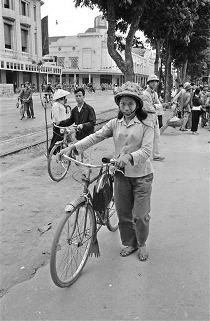 Một phụ nữ dắt xe đạp cạnh đường xe điện bên bờ hồ, phía xa là ngã tư Đinh Tiên Hoàng - Tràng Tiền, 21/3/1973.