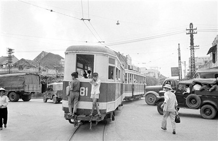 Hai thiếu niên đeo bám sau toa tàu điện bằng gỗ ở trung tâm Hà Nội, 4/4/1973. Không ai bận tậm đến việc xử lý các đối tượng "lậu vé" này.