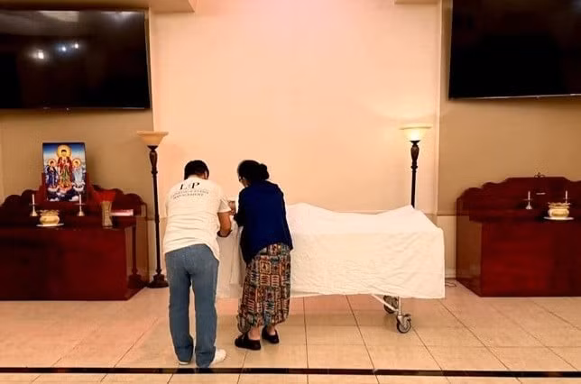 Mẹ Kasim Hoàng Vũ chỉnh sửa lại khăn phủ diện cho con trai tại nhà quàn. Ảnh: FBNV