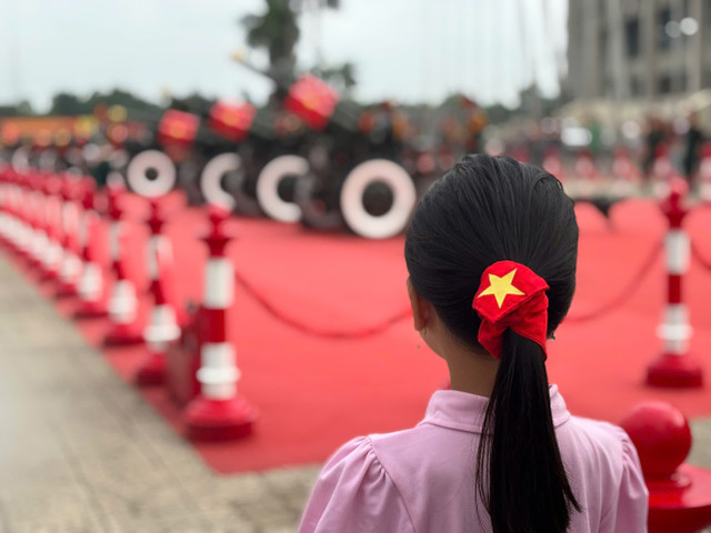 Em bé với chiếc nơ buộc tóc có màu cờ đỏ và ngôi sao vàng 5 cánh đang ngắm nhìn những khí tài quân sự. z6930543741296-6c21896a5613860e538614ed34dada0c.jpg