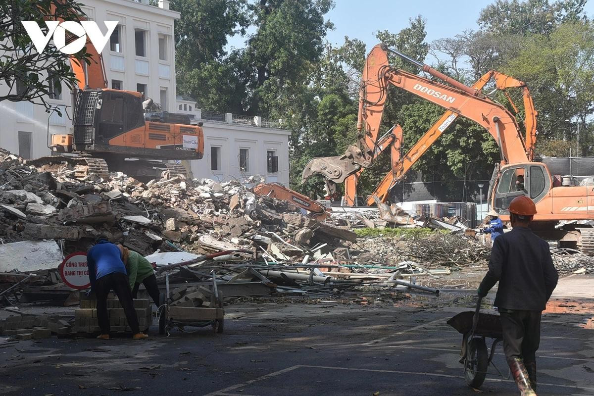 Công nhân làm việc tại công trường phối hợp với máy móc để xử lý và di chuyển vật liệu.