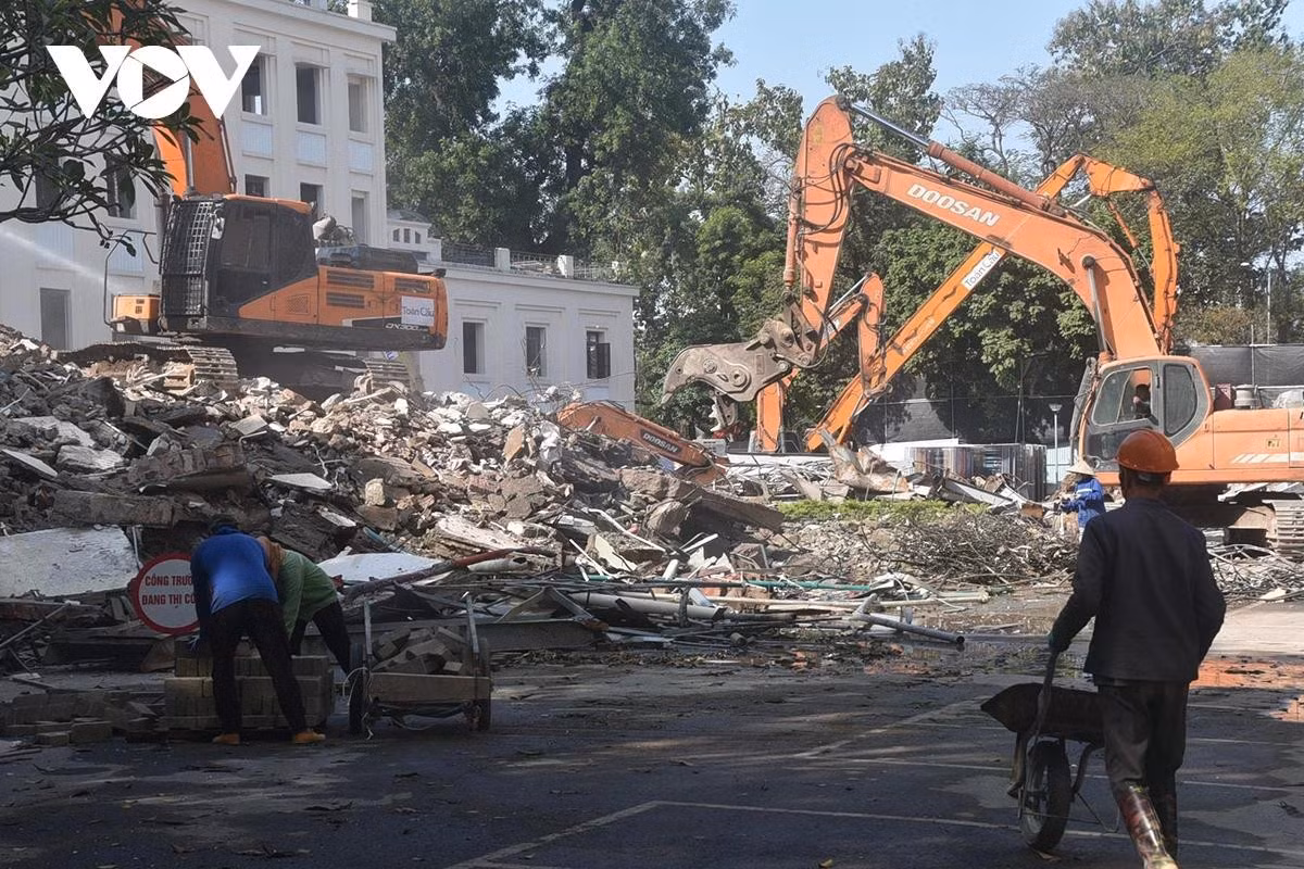 Công nhân làm việc tại công trường phối hợp với máy móc để xử lý và di chuyển vật liệu.