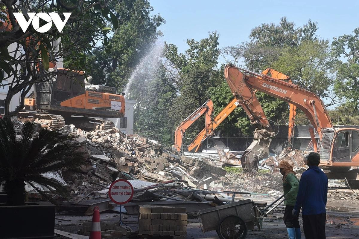 Máy xúc liên tục gạt, gom các khối bê tông và vật liệu xây dựng sau khi công trình bị phá bỏ.