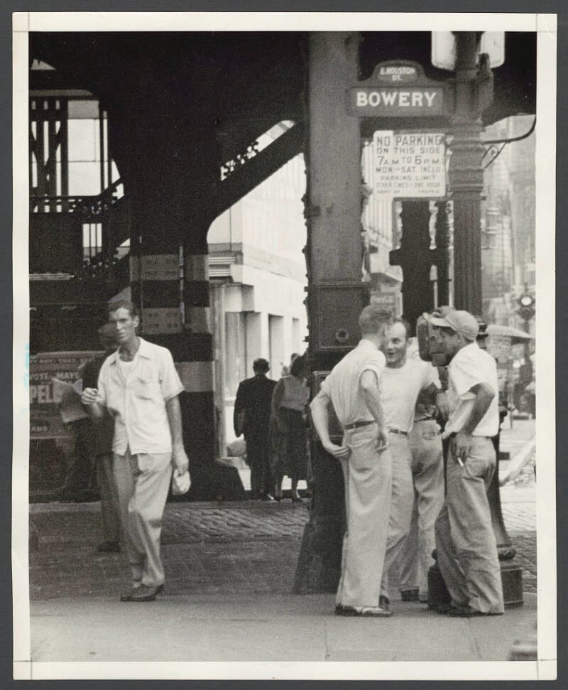 Một nhóm thanh niên đứng trò chuyện ở Bowery năm 1953. Họ đứng bên dưới tuyến đường sắt trên cao.