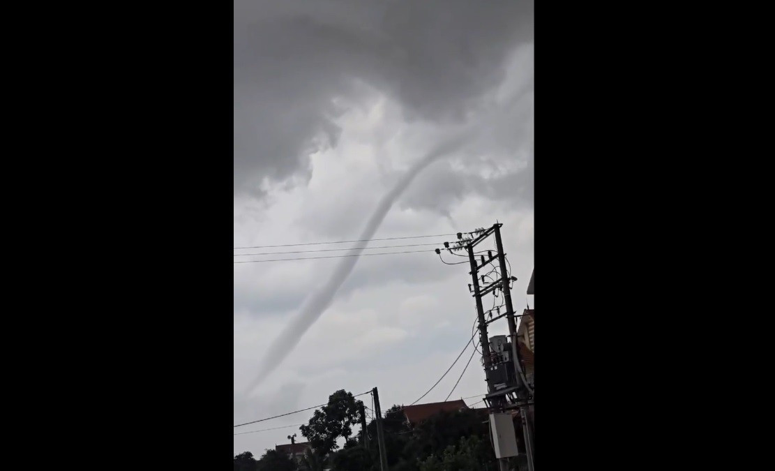 Hiện tượng này kéo dài khoảng 15 phút, với hình dạng đặc trưng là một cột xoáy hình phễu nối từ mặt đất lên một đám mây đen đặc phía trên. Vòi rồng cuộn xoáy dữ dội nhưng nhanh chóng tan biến, không gây thiệt hại về người hay tài sản. Ảnh: Cắt từ clip/Vietnamnet.