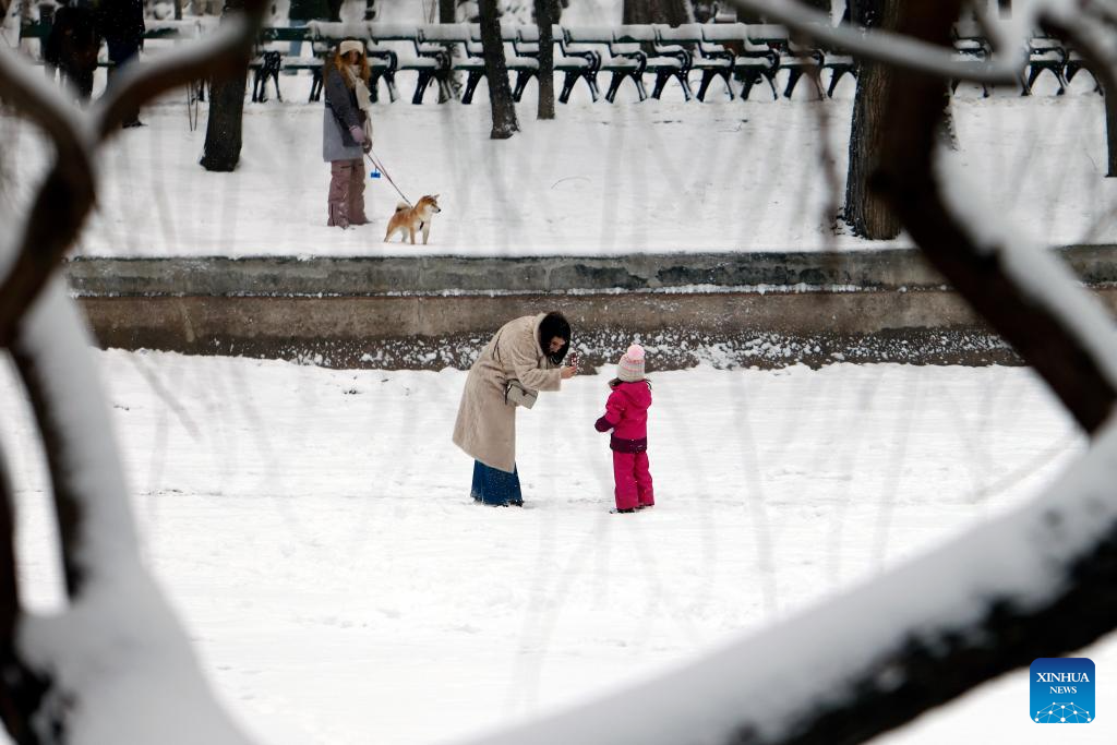 Những bức ảnh được Tân Hoa Xã đăng tải dưới đây phần nào hé lộ cuộc sống của người dân ở Romania giữa mùa đông lạnh giá. Ảnh: Một phụ nữ chụp ảnh cho em nhỏ giữa khung cảnh tuyết rơi tại một công viên ở Bucharest, Romania, ngày 11/1/2026. (Nguồn ảnh: Xinhua)