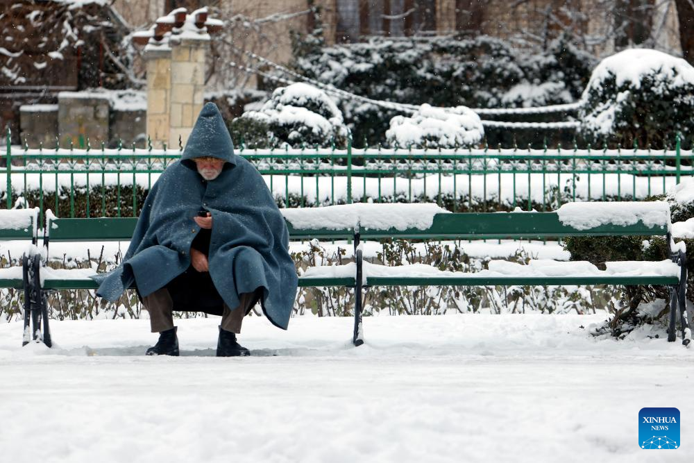 Người đàn ông ngồi nghỉ trên chiếc ghế phủ đầy tuyết trong công viên ở Bucharest ngày 11/1.