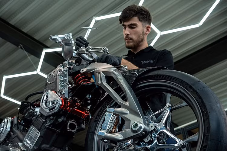 Phần đầu xe là một khối liền mạch tích hợp kính chắn gió và cánh gió khí động học, giúp tăng lực ép xuống mặt đường ở tốc độ cao. So với AMB 001, xe đã được bổ sung cụm đèn trước LED.