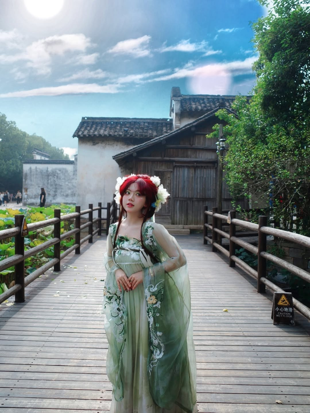 Ánh nắng chiếu nhẹ qua hàng cây, phản chiếu trên mái nhà cổ càng khiến tổng thể trở nên huyền ảo. Bảo Hân đứng giữa lối đi gỗ, dáng vẻ mềm mại và đôi mắt to tròn nhìn xa xăm, khiến người xem liên tưởng đến hình ảnh thiếu nữ thanh thuần trong truyện kiếm hiệp.