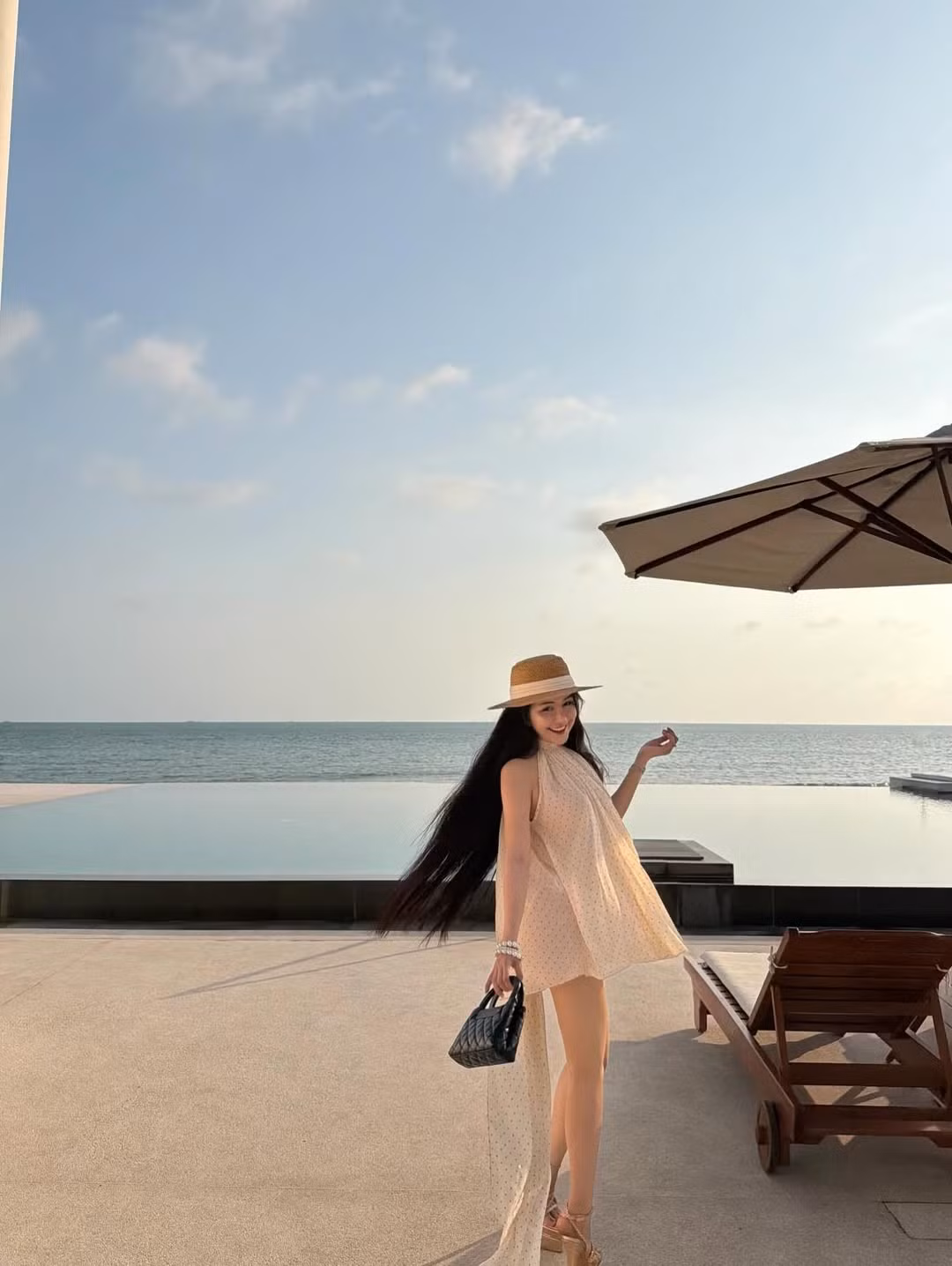 Ở một số khung hình, Võ Ngọc Trân thả dáng trên ghế dài bên hồ bơi, ánh nắng cuối ngày phủ lớp vàng dịu lên mái tóc dài óng ả. Từng cử chỉ như nghiêng đầu, đặt tay nhẹ lên thành ghế hay khẽ xoay người đều toát lên thần thái tự tin, thư thái. Sự kết hợp giữa cảnh sắc thiên nhiên và phong thái người đẹp tạo nên những bức ảnh mang đậm chất thời trang nghỉ dưỡng cao cấp.