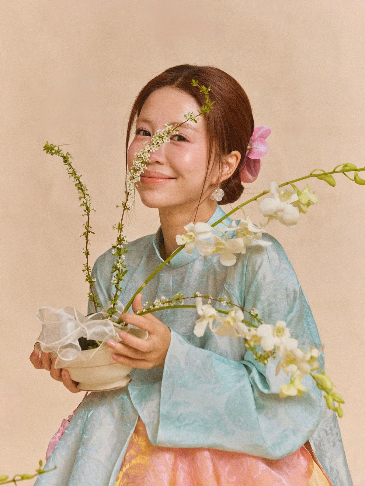 Điểm đặc biệt trong loạt ảnh là cách Mẫn Tiên kết hợp áo dài với những phụ kiện mang đậm tính biểu tượng ngày Tết như hoa tươi, giỏ tre hay những chi tiết trang trí truyền thống.