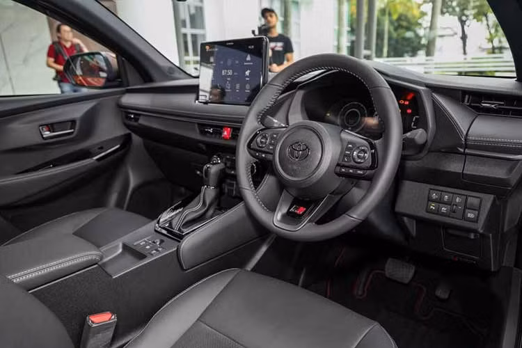 Khoang lái của Vios Hybrid vẫn sử dụng tông màu đen kết hợp đỏ rượu, trang bị bảng táp-lô mềm, ghế da, cùng hệ thống đèn viền 64 màu. Nâng cấp đáng chú ý là màn hình giải trí trung tâm 10,1 inch – lớn hơn bản xăng, hỗ trợ Apple CarPlay/Android Auto không dây, cùng sạc không dây và dàn âm thanh 6 loa.