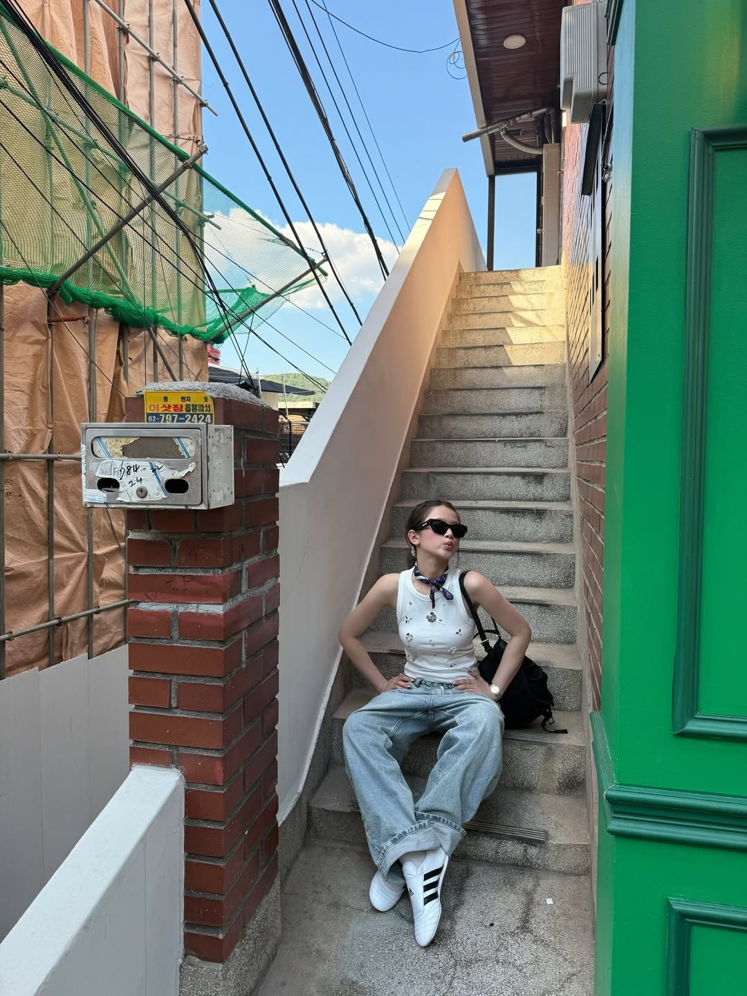 Phụ kiện đi kèm như kính râm đen, khăn buộc cổ nhỏ tạo điểm nhấn tinh tế, mang đến tổng thể năng động nhưng vẫn thời trang.