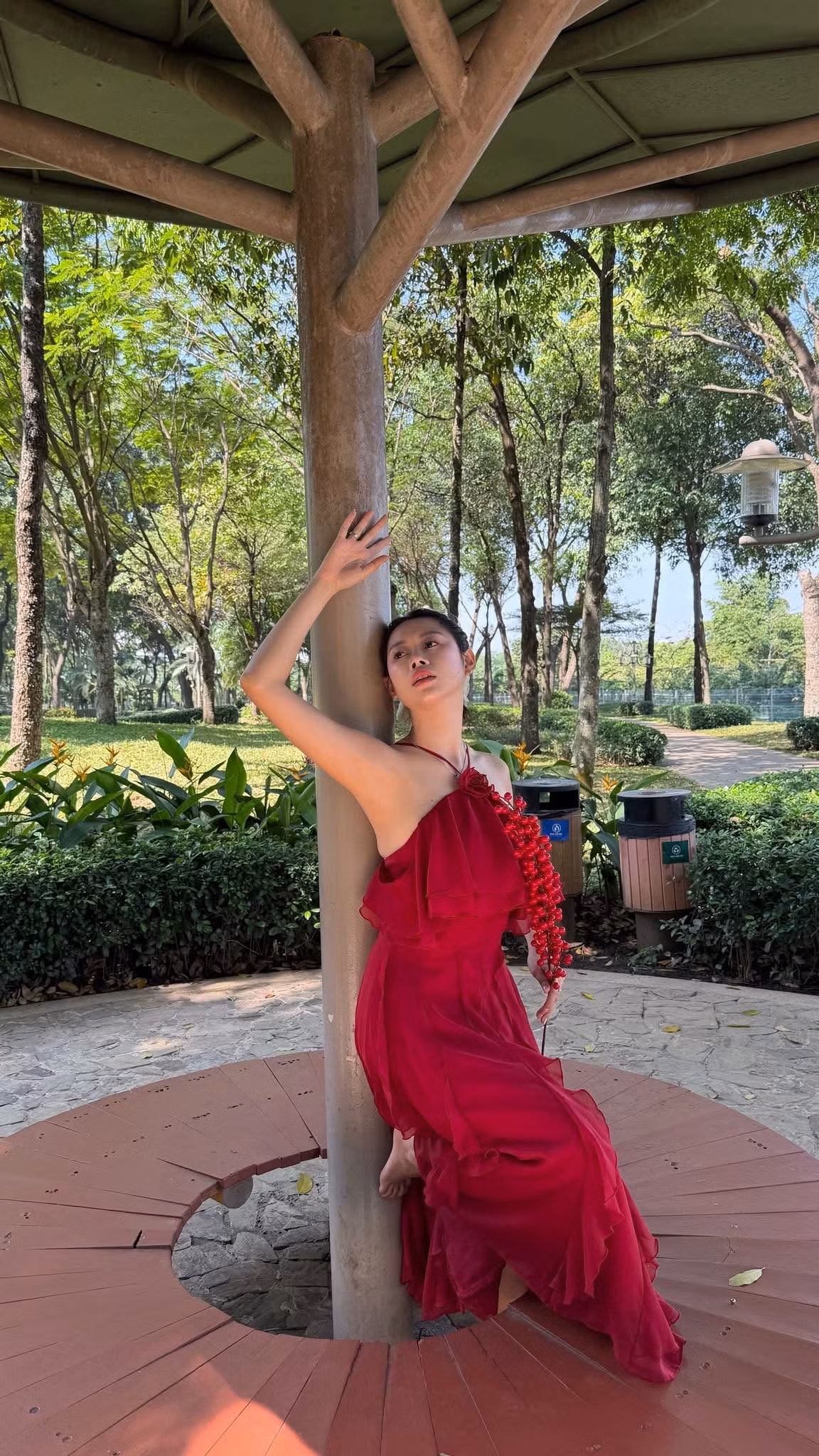 Trong loạt ảnh mới, Việt Phương Thoa diện váy đỏ nổi bật – gam màu đặc trưng của ngày Tết – nhưng thay vì tạo dáng nhẹ nhàng, dịu dàng, cô nàng lại “chơi lớn” với những tư thế chẳng giống ai: đu xà giữa công viên, nằm dài trên lối đi, ôm cây tạo dáng, hay vô tư tập máy thể dục ngoài trời.