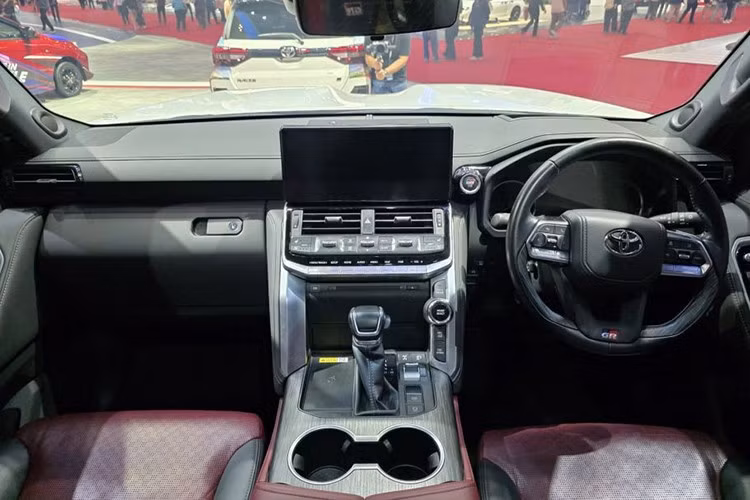 Khoang lái của Toyota Land Cruiser 300 GR Sport kết hợp giữa phong cách sang trọng và tinh thần thể thao. Các chi tiết ốp da màu đen tương phản với đường chỉ đỏ nổi bật, đi kèm logo GR xuất hiện trên vô-lăng, tựa đầu và nút khởi động.