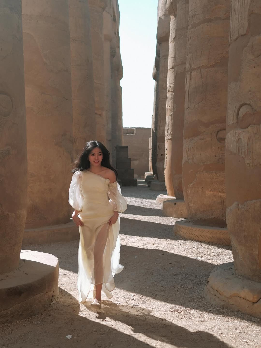 Trong khung cảnh những cột đá khổng lồ phủ đầy dấu tích thời gian, Đỗ Khánh Vân lựa chọn chiếc váy trắng dáng dài, thiết kế lệch vai mềm mại, chất liệu voan mỏng bay bổng.