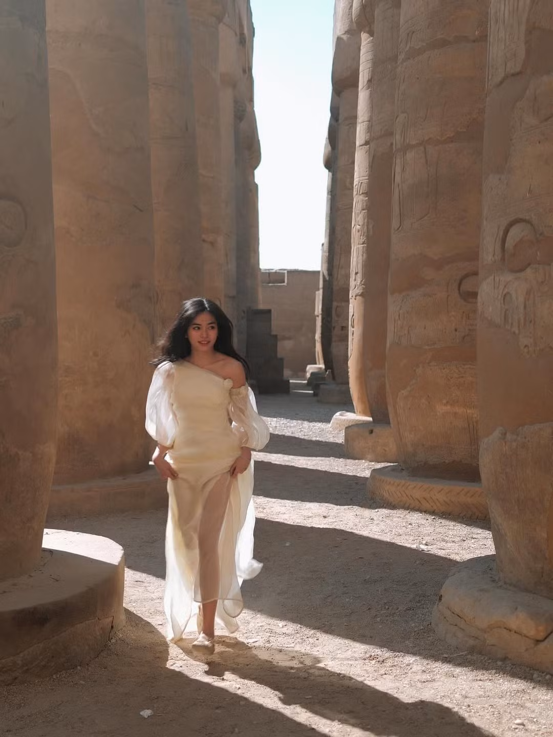 Trong khung cảnh những cột đá khổng lồ phủ đầy dấu tích thời gian, Đỗ Khánh Vân lựa chọn chiếc váy trắng dáng dài, thiết kế lệch vai mềm mại, chất liệu voan mỏng bay bổng.