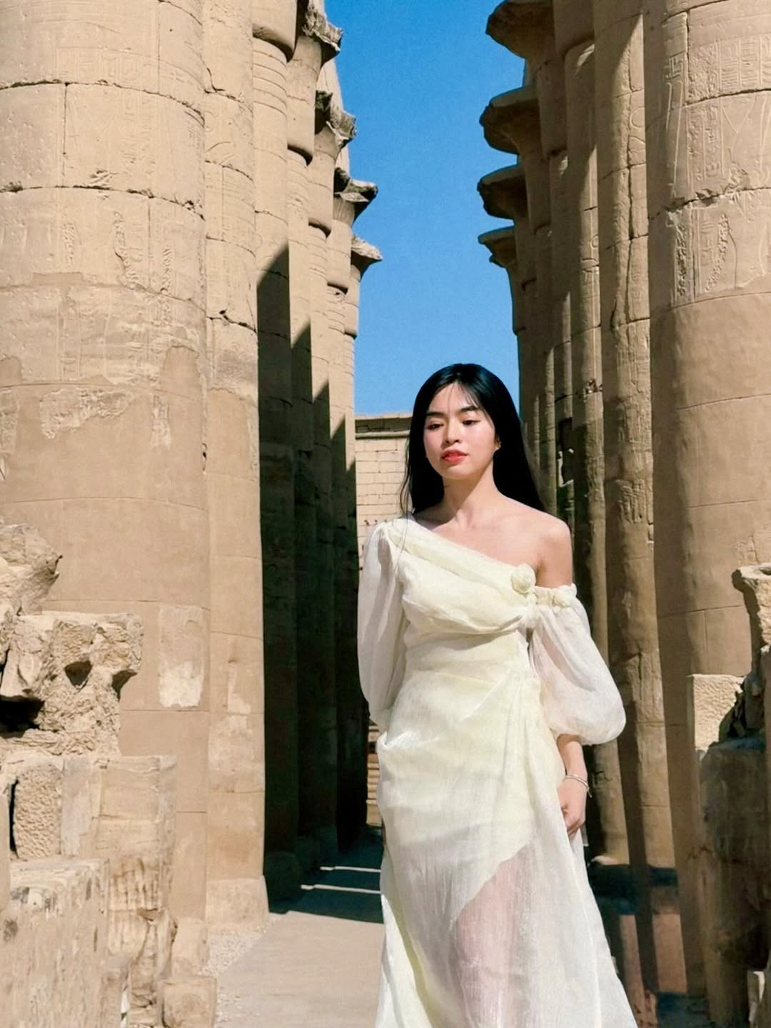 Điểm khiến người xem khó rời mắt chính là thần thái miễn chê của Đỗ Khánh Vân. Khi thì cô thả bước nhẹ nhàng giữa lối đi đá cổ kính, ánh nhìn xa xăm mang chút trầm tư, khi lại nở nụ cười rạng rỡ, để lộ má lúm đồng tiền thương hiệu.