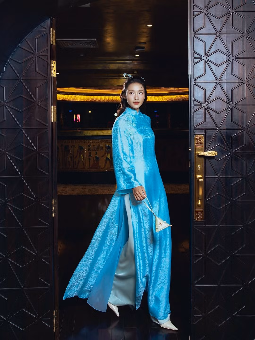 Lựa chọn thiết kế áo dài tông xanh da trời nhẹ nhàng, Khả Ngân khéo léo tôn lên làn da sáng cùng vẻ đẹp trong trẻo vốn có. Phom dáng áo dài suông mềm mại, cổ cao truyền thống, kết hợp cùng họa tiết chìm tinh tế giúp tổng thể vừa thanh lịch vừa hiện đại. Chất liệu vải có độ bắt sáng nhẹ tạo hiệu ứng óng ả, khiến mỗi chuyển động của cô thêm phần uyển chuyển.