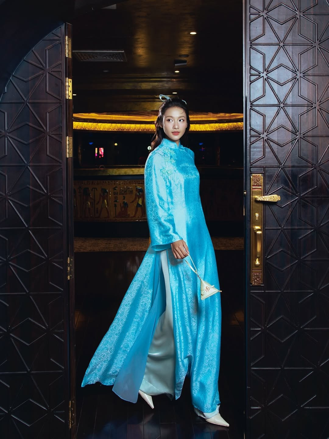 Lựa chọn thiết kế áo dài tông xanh da trời nhẹ nhàng, Khả Ngân khéo léo tôn lên làn da sáng cùng vẻ đẹp trong trẻo vốn có. Phom dáng áo dài suông mềm mại, cổ cao truyền thống, kết hợp cùng họa tiết chìm tinh tế giúp tổng thể vừa thanh lịch vừa hiện đại. Chất liệu vải có độ bắt sáng nhẹ tạo hiệu ứng óng ả, khiến mỗi chuyển động của cô thêm phần uyển chuyển.