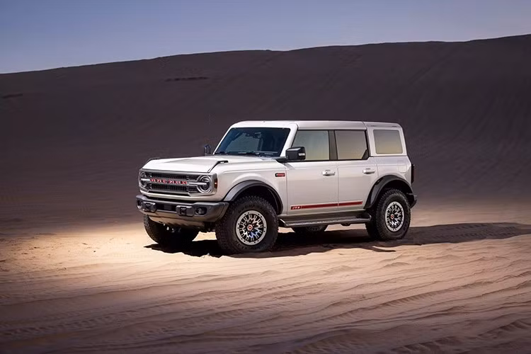 Điểm nhấn của mặt trước Ford Bronco 2026 bản kỷ niệm là ngoại thất sơn màu trắng, dòng chữ “BRONCO” sơn màu đỏ - Vermilion Red hiện đại. Lưới tản nhiệt mới lấy cảm hứng từ thiết kế gốc nhưng kết hợp sơn Warm Alloy. Đây là tông màu lịch sử của Ford có trên Bronco.