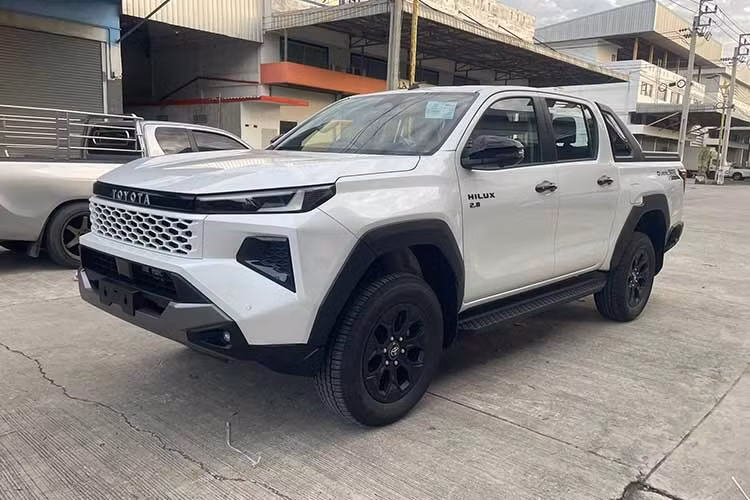 Ở thế hệ mới, Hilux 2026 sở hữu diện mạo mạnh mẽ và hiện đại hơn với ngôn ngữ thiết kế “Cyber Sumo”. Phần đầu xe nổi bật với lưới tản nhiệt cỡ lớn, kết hợp cụm đèn LED tạo hình sắc sảo, trong khi khu vực phía sau được tinh chỉnh với đèn hậu LED đồ họa mới, cản sau thiết kế lại và tay nắm thùng hàng mới.