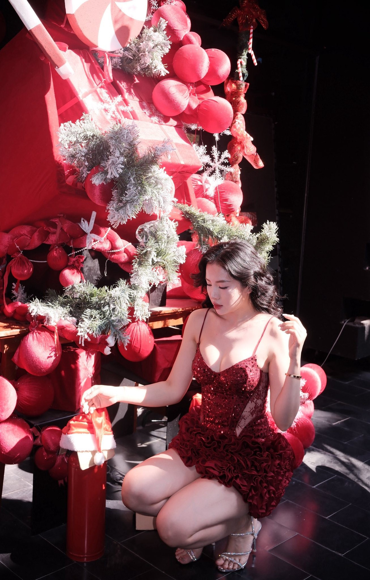 Gam màu đỏ rực rỡ đặc trưng của mùa Noel không chỉ giúp cô nổi bật giữa không gian trang trí đậm chất lễ hội, mà còn tôn lên làn da trắng mịn và đường cong mềm mại. Cách phối cùng giày cao gót quai mảnh càng làm tổng thể thêm phần nữ tính, quyến rũ nhưng vẫn giữ được sự tinh tế.