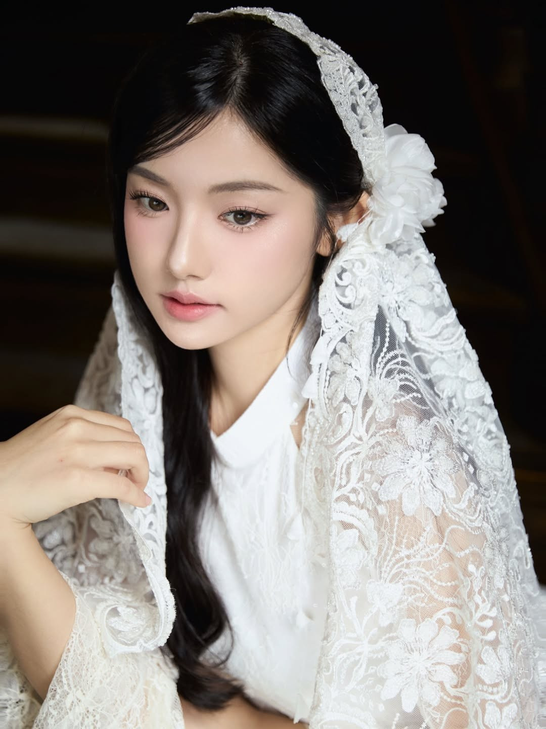 Điểm đặc biệt làm nên “linh hồn” của bộ ảnh chính là chiếc khăn voan ren phủ nhẹ trên mái tóc đen dài. Phụ kiện này gợi liên tưởng đến hình ảnh cô dâu cổ điển hay những thiếu nữ xưa trong tranh lụa, tạo nên vẻ đẹp vừa thuần khiết vừa có chút hoài niệm. Khi Quỳnh Trương khẽ đưa tay giữ mép khăn, từng chuyển động nhỏ cũng trở nên mềm mại, đầy nữ tính.