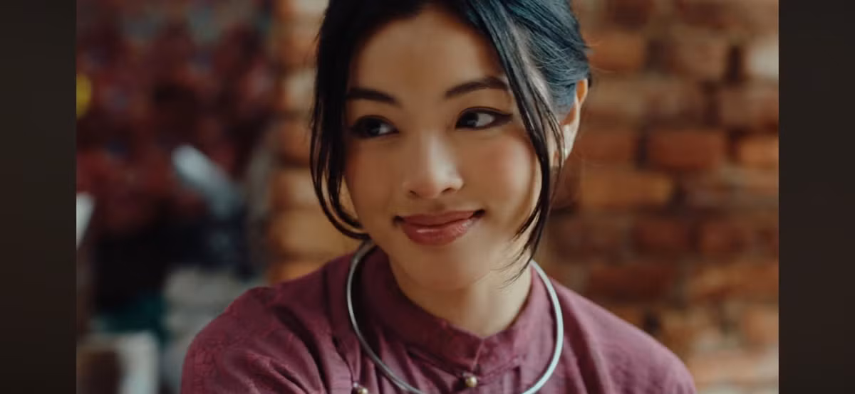 Trong một phân cảnh, an Thy ngồi trên ghế gỗ, tay cầm quạt nan (hoặc nón lá) che mặt, tạo dáng quý phái, đối lập với sự "ngông" của hai nam chính đứng xung quanh. Ở một cảnh khác, cô ngồi trên chiếu cói, cúi người xem bói, hành động đầy bí ẩn và cuốn hút.