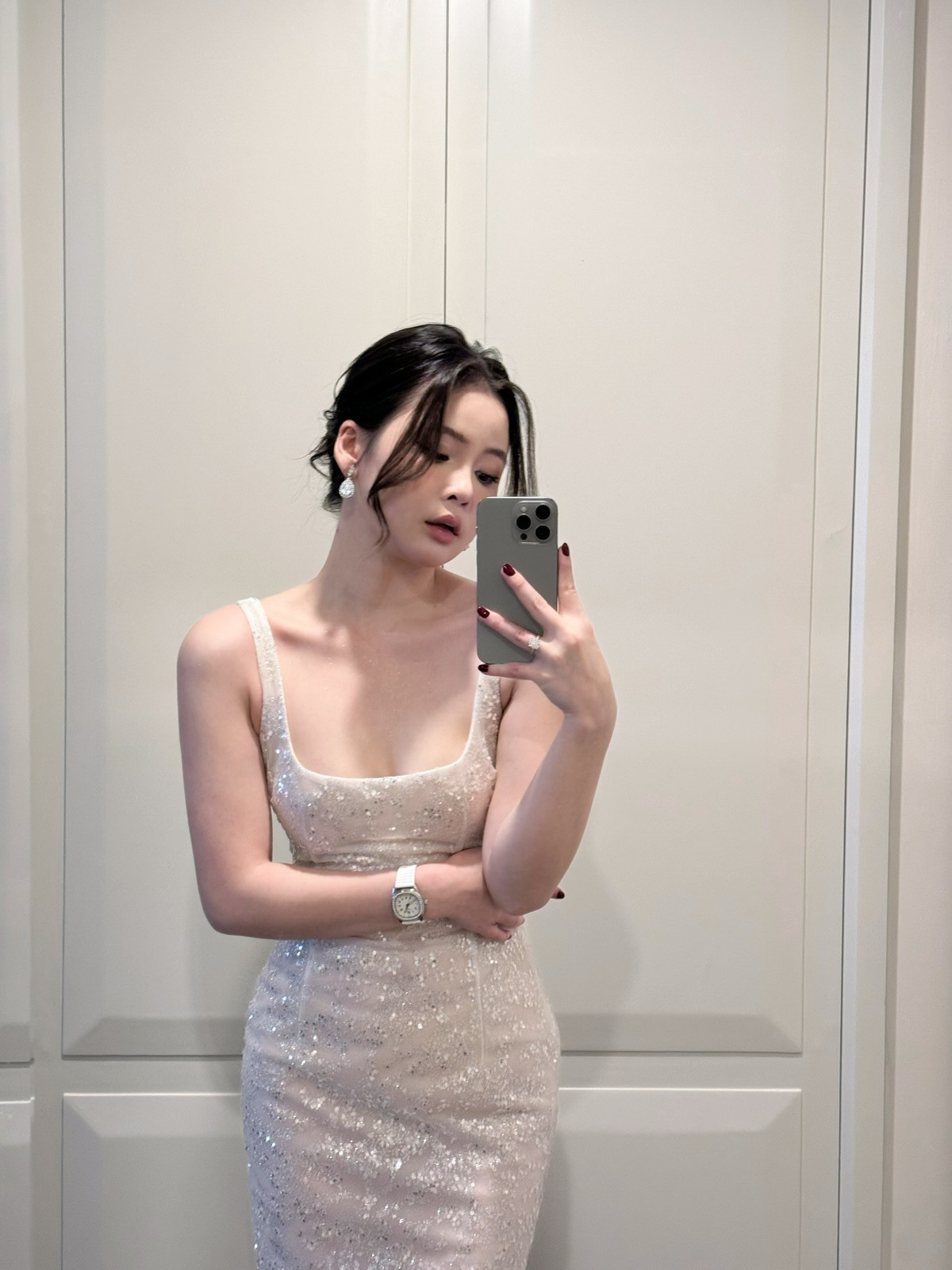 Nổi bật trong ảnh là làn da trắng mịn, mái tóc được buộc gọn kết hợp vài lọn tóc nhẹ buông trước trán, tạo nên vẻ đẹp vừa ngây thơ vừa quyến rũ. Ánh sáng bữa tiệc lung linh hòa cùng backdrop hoa được trang trí tinh tế càng khiến tổng thể khung hình trở nên sang trọng, tôn trọn nhan sắc “miễn chê” của nàng hot girl.