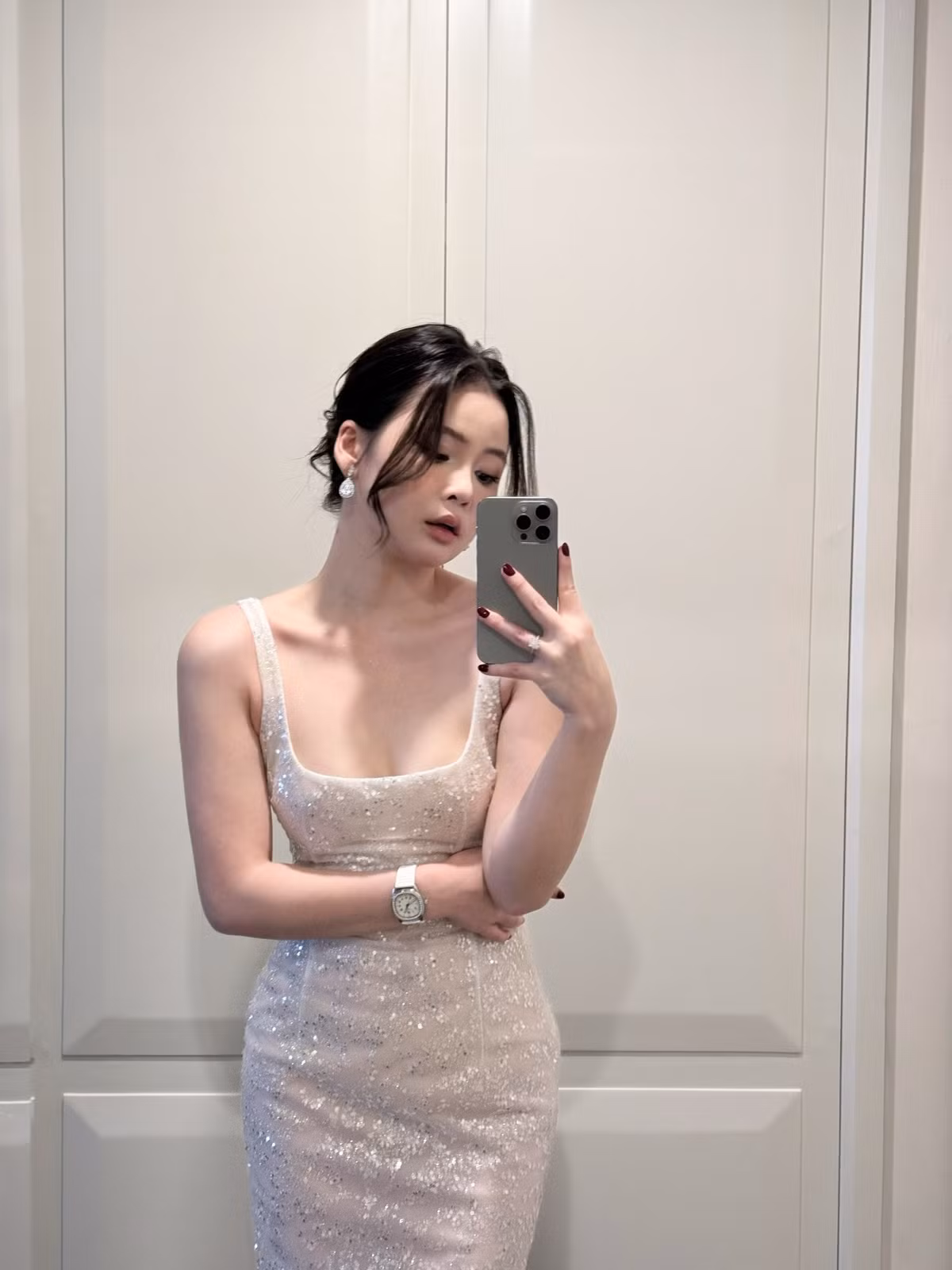 Nổi bật trong ảnh là làn da trắng mịn, mái tóc được buộc gọn kết hợp vài lọn tóc nhẹ buông trước trán, tạo nên vẻ đẹp vừa ngây thơ vừa quyến rũ. Ánh sáng bữa tiệc lung linh hòa cùng backdrop hoa được trang trí tinh tế càng khiến tổng thể khung hình trở nên sang trọng, tôn trọn nhan sắc “miễn chê” của nàng hot girl.