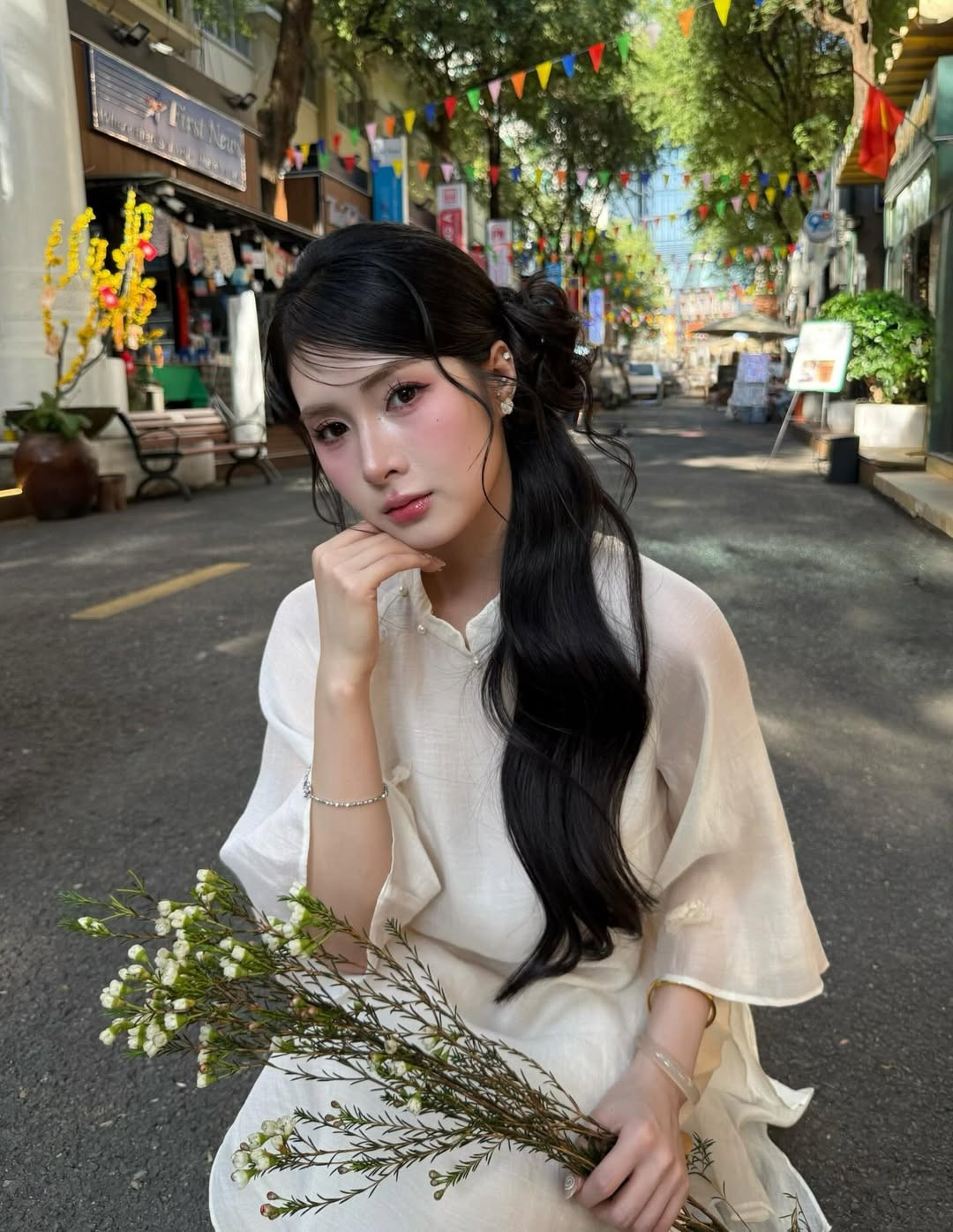 Giữa không gian phố xá treo cờ, đèn rực rỡ, hình ảnh Quỳnh Alee ôm bó hoa nhỏ, ngồi trên ghế gỗ hay dạo bước giữa con đường yên ả mang đến cảm giác vừa thơ mộng vừa gần gũi.