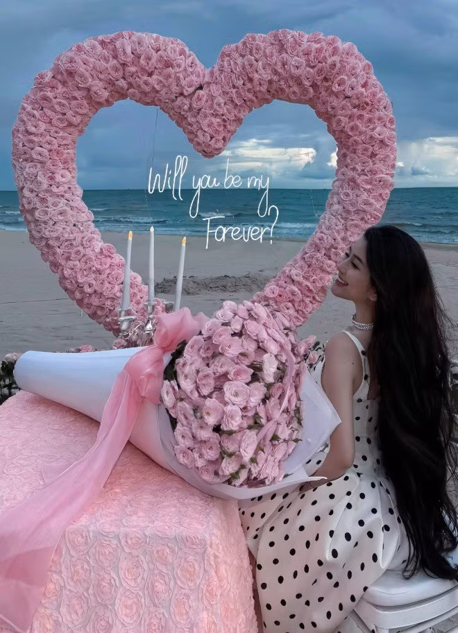 Không gian trong ảnh của Võ Ngọc Trân được trang trí bằng hàng nghìn đóa hồng pastel xếp thành trái tim khổng lồ hướng ra biển, trên bàn phủ khăn hoa tinh xảo, bó hoa hồng cùng nến trắng lung linh, tạo nên bầu không khí ngọt ngào.