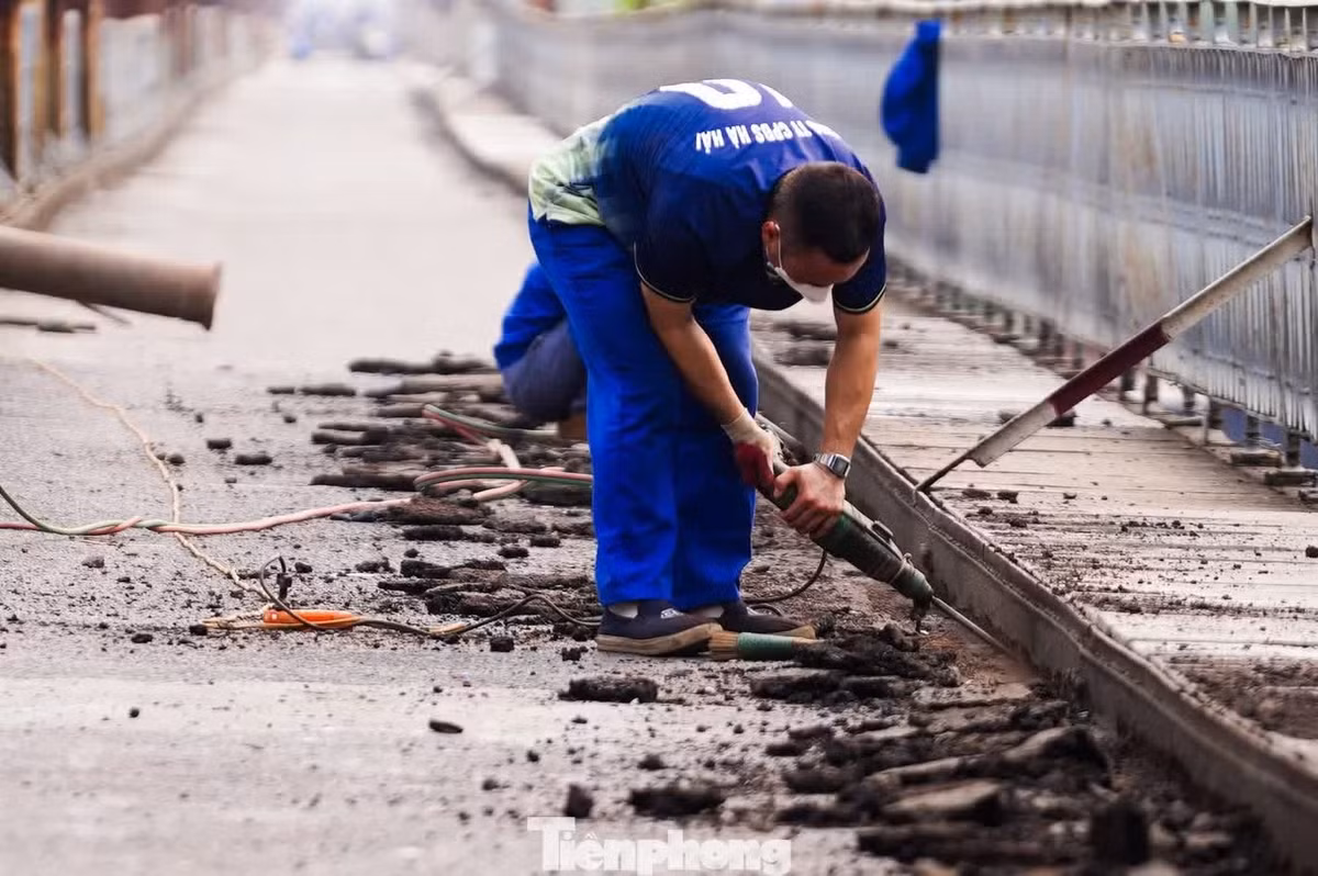 Công nhân đang khoan, đục tại khu vực mép lan can cầu nhằm xử lý phần kết cấu cũ, tạo mặt bằng kỹ thuật phục vụ công tác gia cố và lắp đặt, hoàn thiện hệ thống thoát nước.