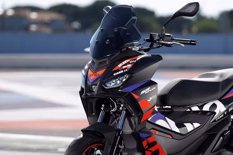 SR GT 200 Replica gây ấn tượng với thân xe màu đen mờ, kết hợp cùng các chi tiết đồ họa màu đỏ và tím nổi bật. Logo Aprilia cỡ lớn được bố trí tinh tế hai bên thân xe, trong khi bộ mâm trước sơn đen với viền đỏ tạo điểm nhấn mạnh mẽ, tôn vinh hình ảnh của RS-GP trong các cuộc đua MotoGP.