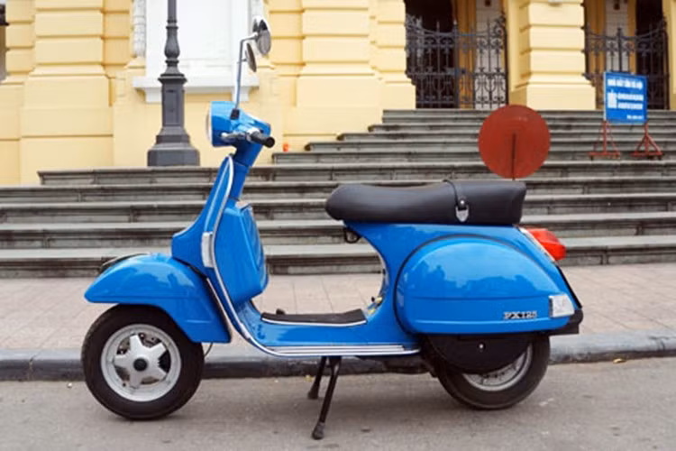 Phần yên xe vẫn còn được bọc nilon nguyên bản, như một lời khẳng định về độ mới đến khó tin. Đèn pha tròn cổ điển, chắn bùn cao, bánh nhỏ đặc trưng, bộ gá chở hàng phía sau bằng inox sáng bóng… tất cả tạo nên một tổng thể hoàn hảo của dòng Vespa PX, biểu tượng thời trang bất hủ của nước Ý.