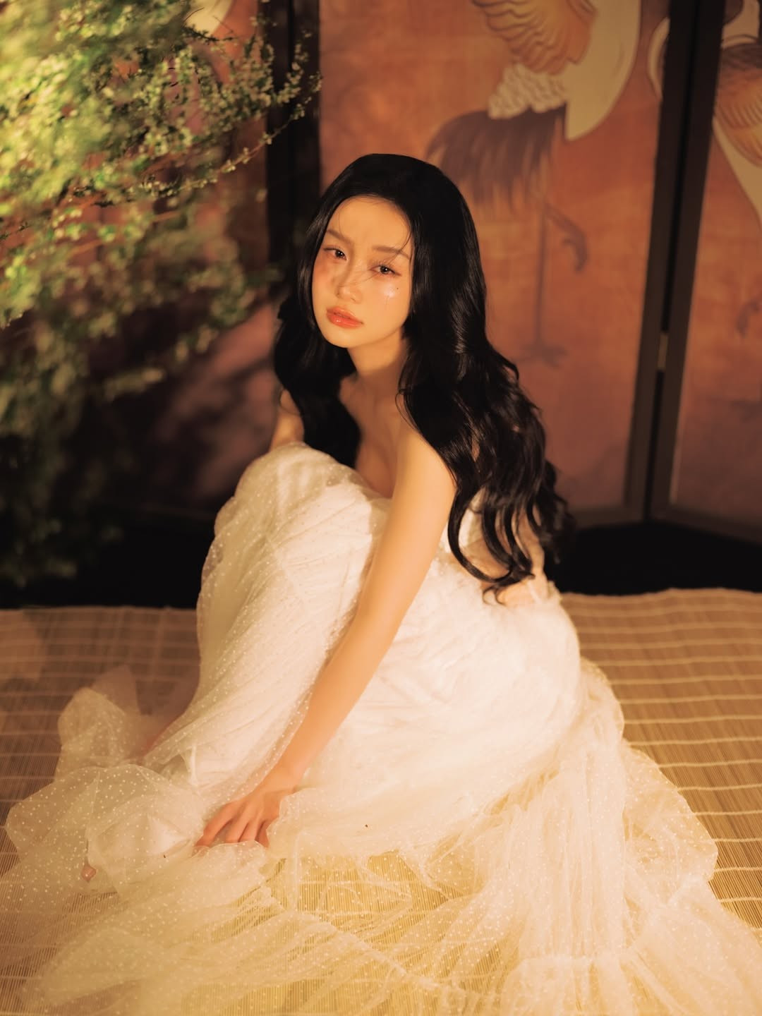 Trong loạt hình mới được chia sẻ, Jun Vũ lựa chọn phong cách nhẹ nhàng nhưng không kém phần quyến rũ. Người đẹp diện thiết kế váy trắng xuyên thấu nhiều lớp voan mềm mại, tạo hiệu ứng bồng bềnh như mây. Chất liệu mỏng nhẹ kết hợp phom dáng corset ôm sát giúp tôn lên vóc dáng thanh mảnh, đồng thời mang lại cảm giác mong manh, thuần khiết – đúng với hình ảnh “bạch trà” mà cô tự ví von.