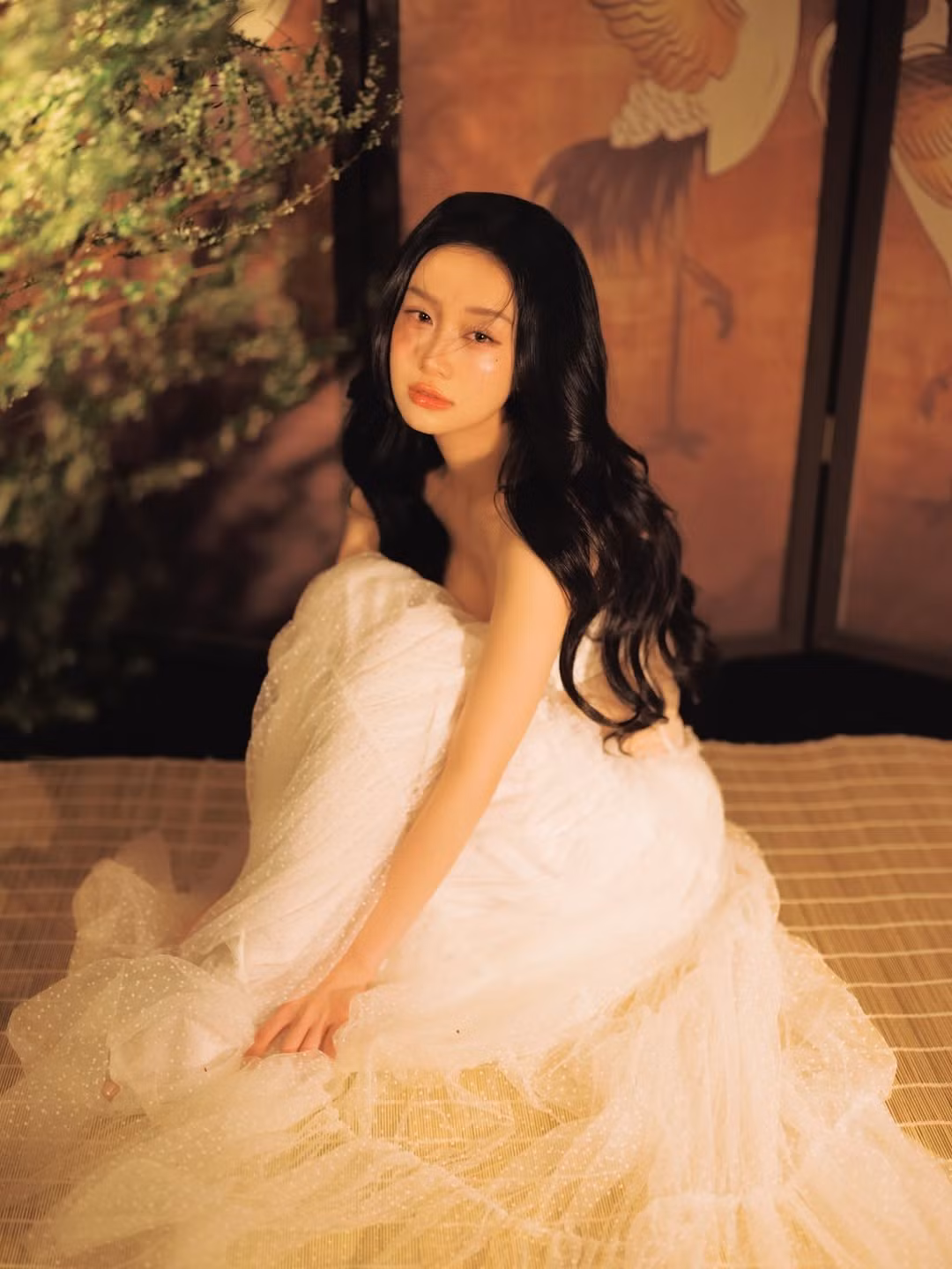 Trong loạt hình mới được chia sẻ, Jun Vũ lựa chọn phong cách nhẹ nhàng nhưng không kém phần quyến rũ. Người đẹp diện thiết kế váy trắng xuyên thấu nhiều lớp voan mềm mại, tạo hiệu ứng bồng bềnh như mây. Chất liệu mỏng nhẹ kết hợp phom dáng corset ôm sát giúp tôn lên vóc dáng thanh mảnh, đồng thời mang lại cảm giác mong manh, thuần khiết – đúng với hình ảnh “bạch trà” mà cô tự ví von.