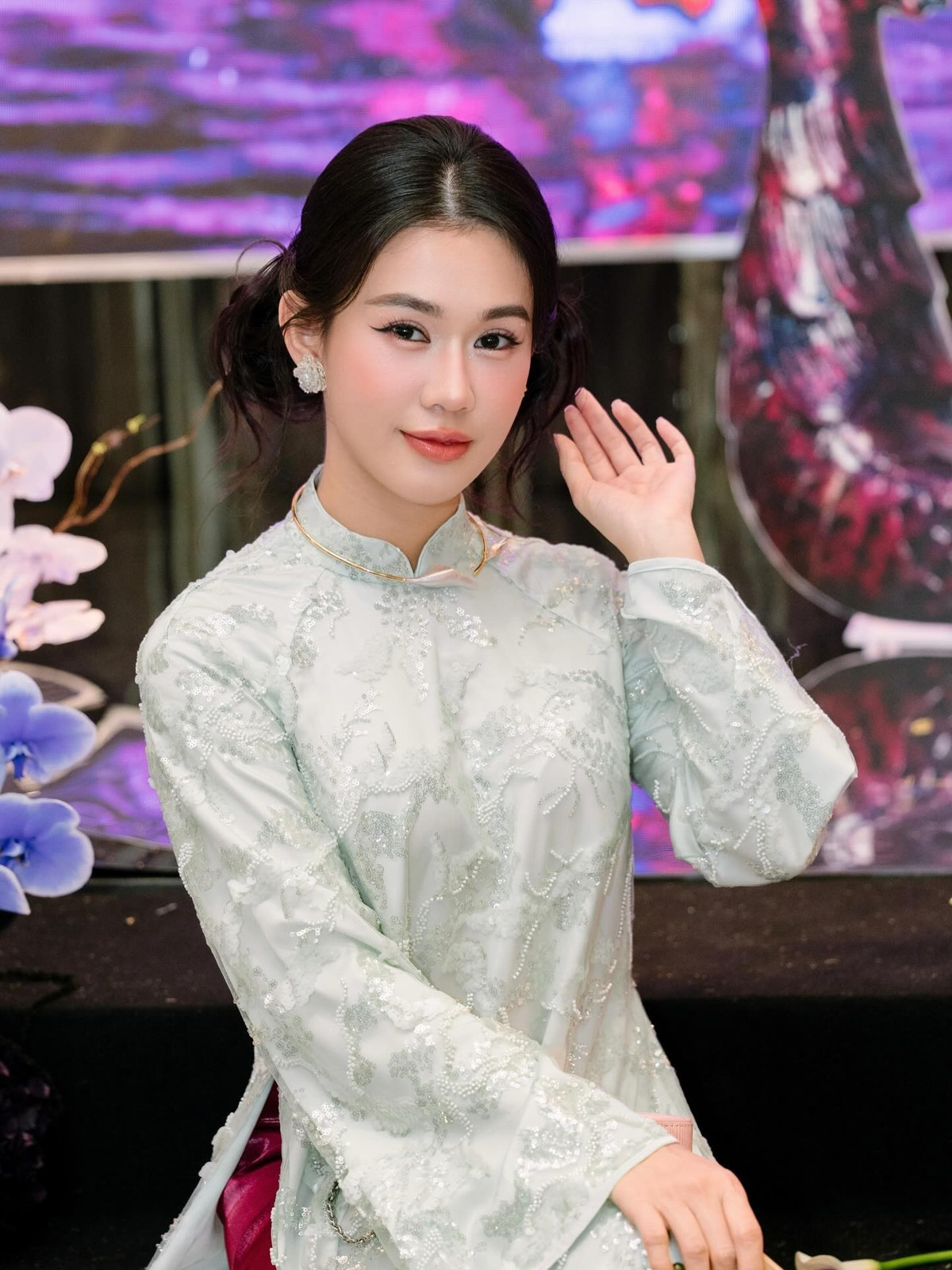 Trong loạt ảnh được chia sẻ, Ngọc Thảo diện áo dài tông xanh pastel nhẹ nhàng, chất liệu thêu ánh kim tinh tế, tạo hiệu ứng mềm mại và sang trọng. Thiết kế cổ cao, tay dài cùng phom dáng suông truyền thống giúp tôn lên vóc dáng thanh thoát dù cô chỉ cao 1m62. Khi kết hợp cùng quần lụa hồng trầm và phụ kiện quạt tay, tổng thể trang phục mang đến cảm giác nền nã, hoài cổ nhưng không kém phần cuốn hút.