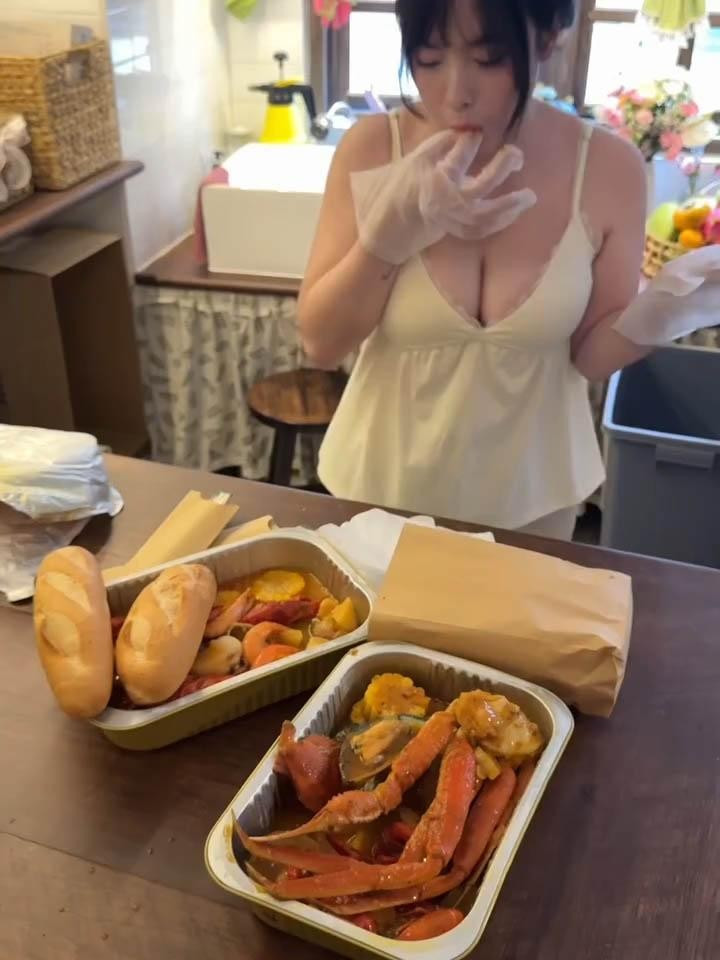 Trong video, Duyên Nguyễn xuất hiện trong một chiếc váy hai dây màu kem nhẹ nhàng, ngồi trước bàn ăn với hai hộp hải sản hoặc món ăn nóng hổi có màu sắc bắt mắt, kèm theo ổ bánh mì dài.