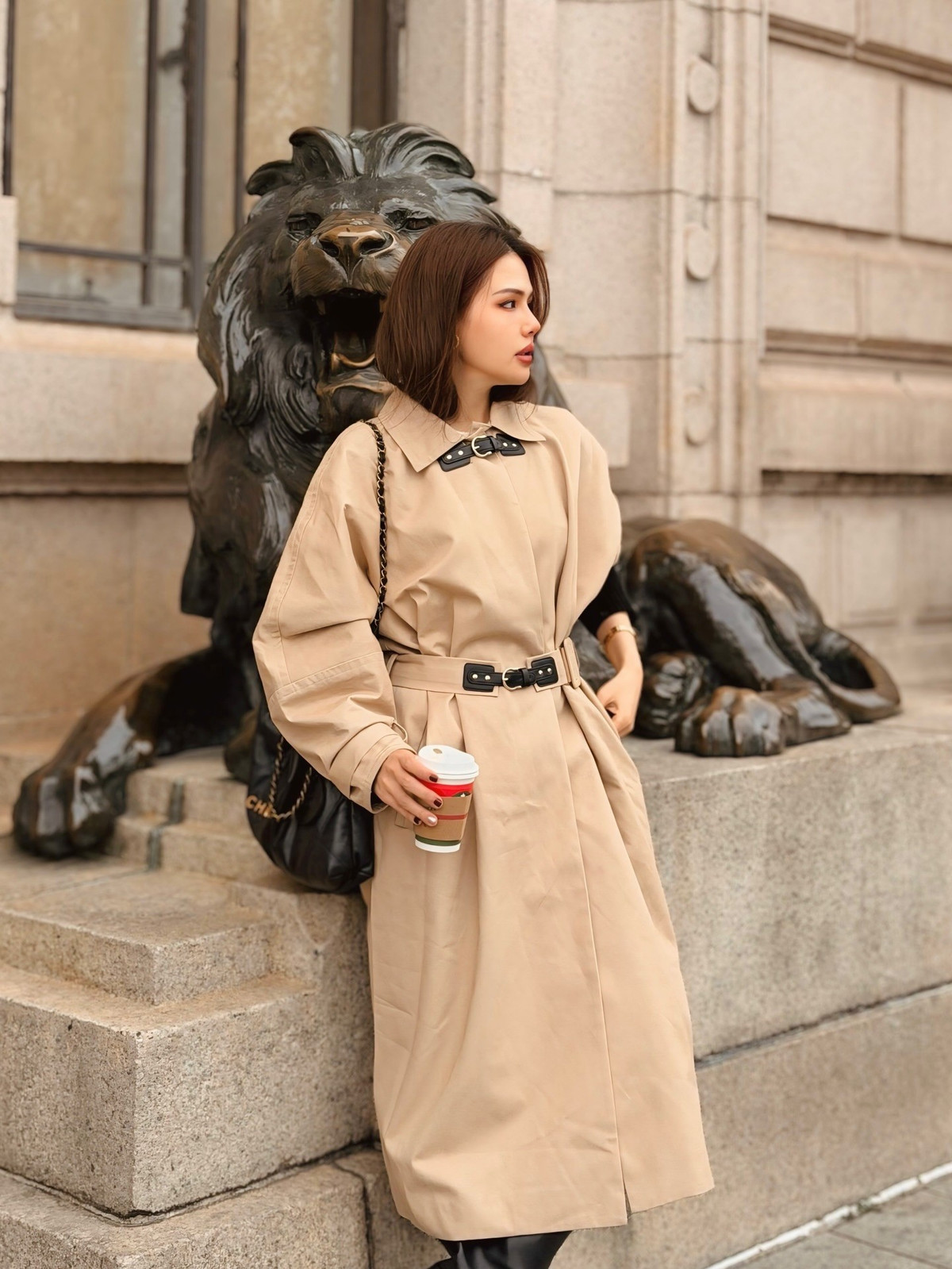 Thiết kế áo khoác dáng dài, thắt eo nhẹ giúp tôn lên vóc dáng thon gọn của nữ diễn viên. Cô phối cùng áo len đen bên trong, túi xách da tông trầm và phụ kiện kim loại ánh vàng, tạo nên tổng thể vừa thanh lịch vừa hiện đại.