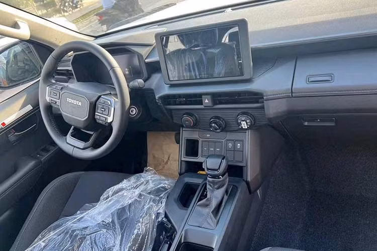 Bên trong, nội thất Hilux 2026 mang thiết kế hiện đại tương tự dòng Land Cruiser, nổi bật với bảng táp-lô trải ngang và cụm màn hình kép 12,3 inch: một cho hệ thống giải trí trung tâm và một cho cụm đồng hồ kỹ thuật số trước vô-lăng.