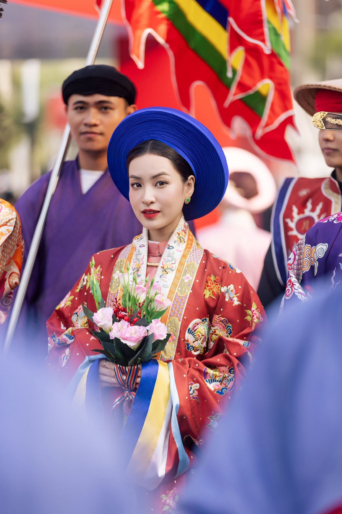 Bên cạnh trang phục, bó hoa cầm tay với sắc hồng nhạt và điểm xuyết quả đỏ nhỏ tạo nên sự cân bằng màu sắc tinh tế. Chi tiết này không chỉ giúp tổng thể bớt “nặng” mà còn mang đến nét mềm mại, nữ tính. Cách cô nâng bó hoa bằng hai tay, dáng đứng thẳng lưng, vai thả lỏng càng làm tăng thêm phong thái nền nã, đúng tinh thần của trang phục truyền thống.